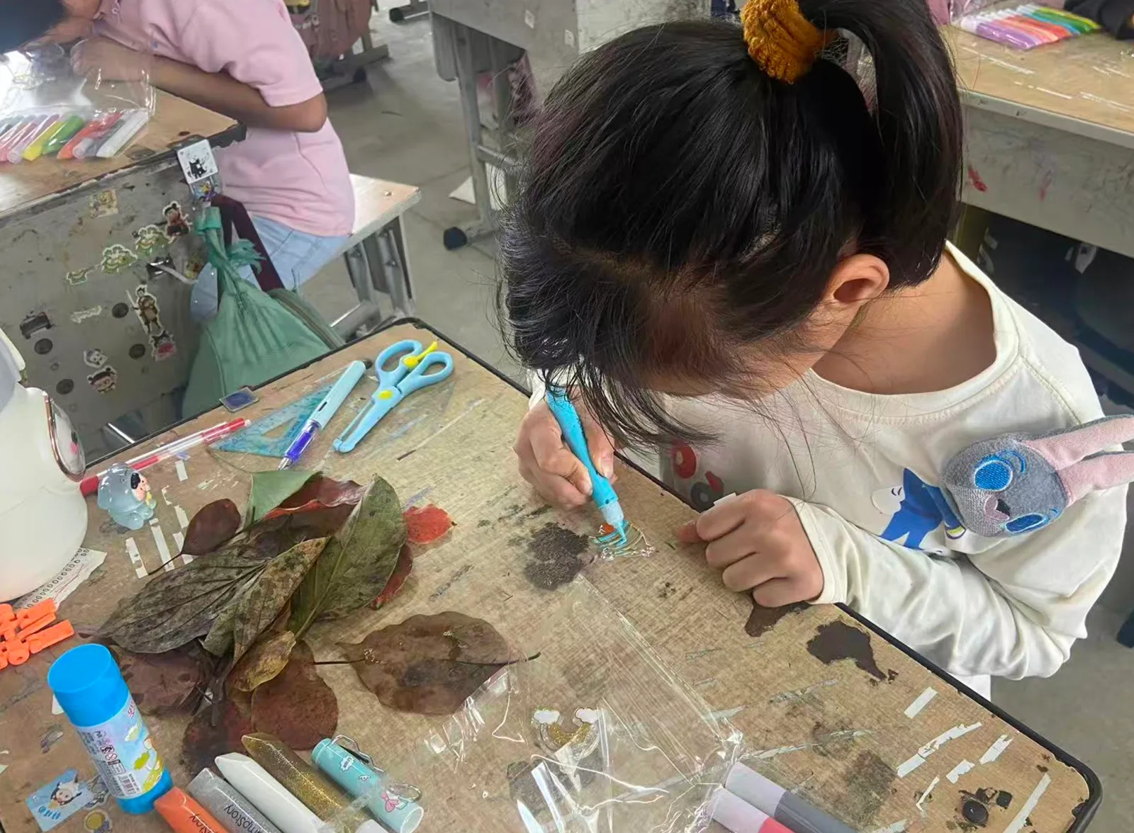 孩子伏在桌前，用蓝色画笔认真制作水彩胶画